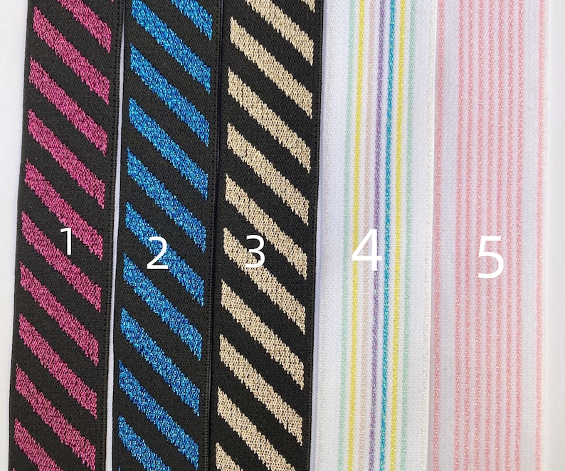 May include: Five samples of elastic trim with different patterns. Sample 1 is black with pink diagonal stripes. Sample 2 is black with blue diagonal stripes. Sample 3 is black with gold diagonal stripes. Sample 4 is white with multi-colored vertical stripes. Sample 5 is white with pink vertical stripes.