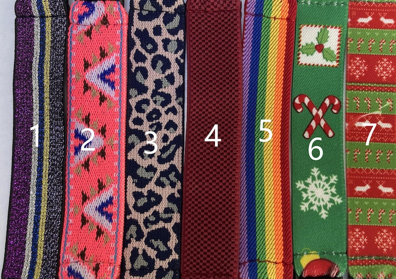 May include: A collection of seven colorful straps with various patterns. Designs include stripes, geometric shapes, leopard print, a woven texture, a rainbow, and Christmas-themed patterns with candy canes and holly.