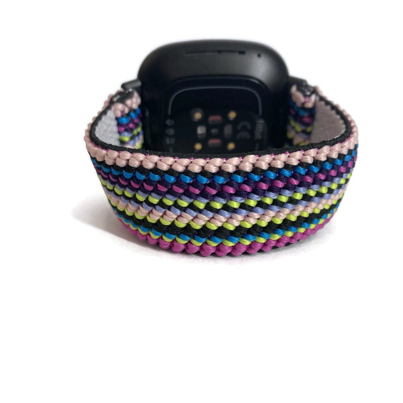 Pode incluir: Uma pulseira de rel&oacute;gio tecida colorida com listras rosa, roxas, azuis, verdes e pretas. A pulseira &eacute; feita de um material macio e flex&iacute;vel e &eacute; projetada para se ajustar a uma variedade de smartwatches.