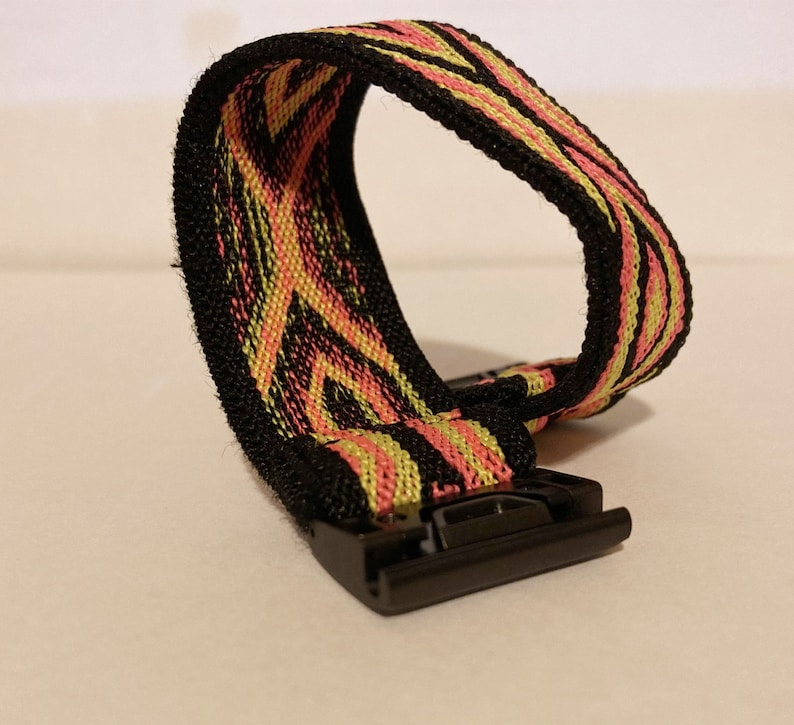 Op de afbeelding: Een zwart horlogebandje met een roze en geel gestreept patroon. Het bandje heeft een zwarte metalen gesp.