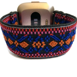 Op de afbeelding: Een zwart elastisch horlogebandje met een kleurrijk geometrisch patroon in rood, oranje, blauw en roze. Het bandje is ontworpen om te passen op een smartwatch.