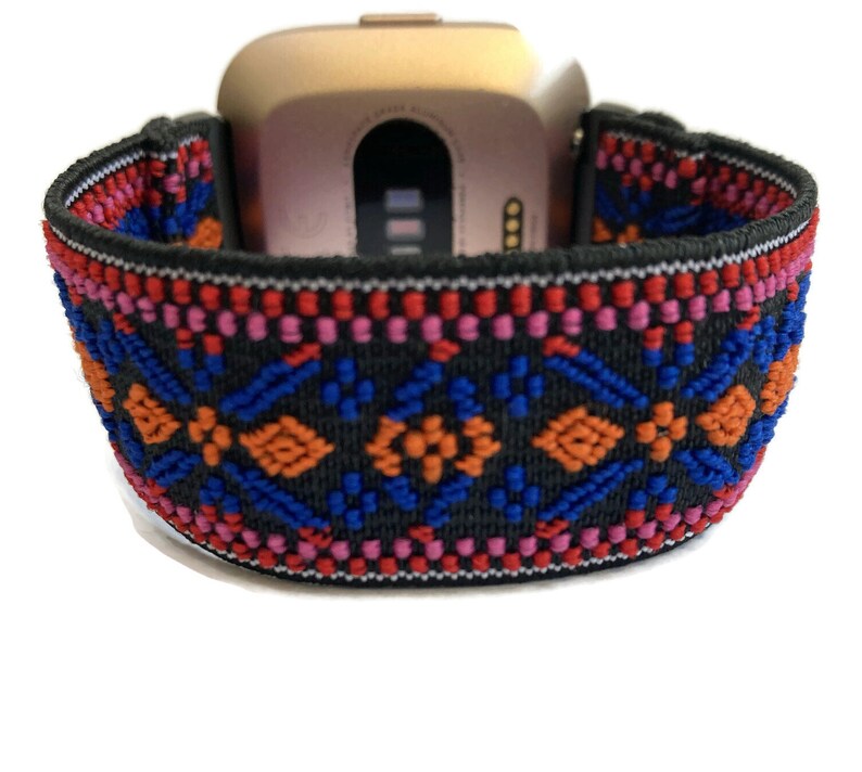 Op de afbeelding: Een zwart elastisch horlogebandje met een kleurrijk geometrisch patroon in rood, oranje, blauw en roze. Het bandje is ontworpen om te passen op een smartwatch.