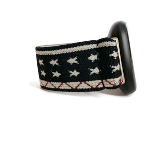 May include: A black and white patterned elastic band with white stars and red stitching. The band is attached to a black plastic object.