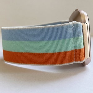 May include: A striped watch band with blue, green, and orange stripes. The band is made of a soft, stretchy material and is compatible with smartwatches.