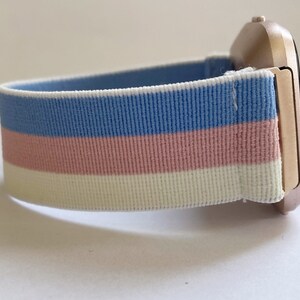 May include: A rose gold smartwatch with a blue, pink, and white striped elastic band.