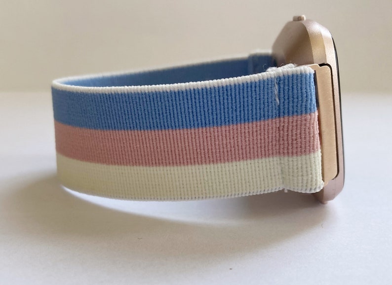 May include: A rose gold smartwatch with a blue, pink, and white striped elastic band.