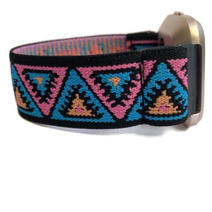 May include: A black elastic watch band with a geometric pattern in pink, blue, and orange. The band is attached to a silver watch face.