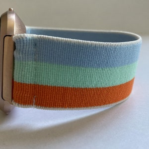May include: A rose gold smartwatch with a striped blue, green, and orange elastic band.
