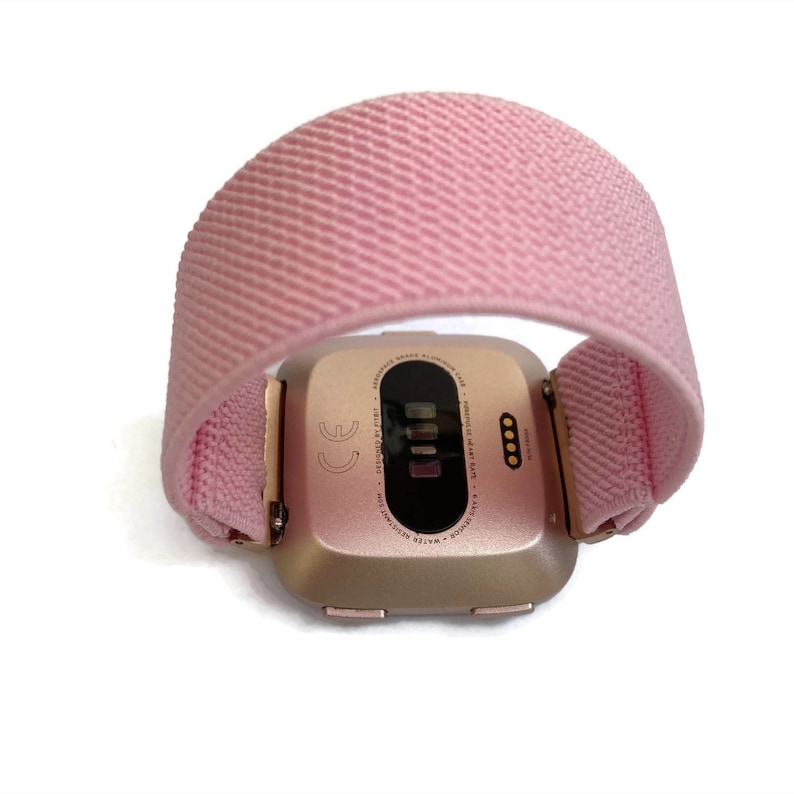 May include: A rose gold smartwatch with a pink band. The back of the watch has a black screen with white text that reads "WATER RESISTANT 5ATM -  DISCOVER FIT -  PERSONALIZE HEART RATE -  MADE ALUMINUM CASE -  GOOGLE ASSISTANT -  BLUETOOTH 4.0 -  CE".