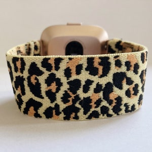 May include: A light beige elastic watch band with a leopard print pattern in black and orange. The band is designed for a smartwatch.