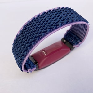 Op de afbeelding: Een geweven fitness tracker band in paars en donkerblauw. De band is gemaakt van een zacht, ademend materiaal en is ontworpen om comfortabel te dragen.