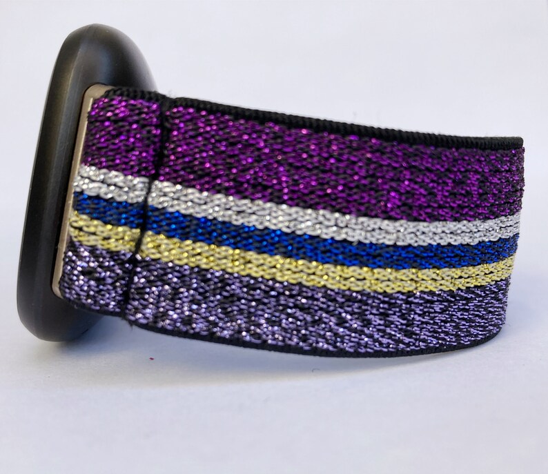 Puede incluir: Una correa de reloj negra y morada con rayas plateadas, azules y doradas. La correa est&aacute; hecha de un material brillante.