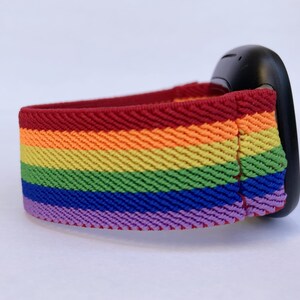 May include: A rainbow-striped elastic band, featuring red, orange, yellow, green, blue, and purple colors. The band is attached to a black object, possibly a wearable device. The band's design is a vibrant display of color.