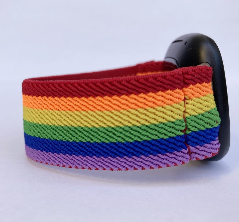 May include: A rainbow-striped elastic band, featuring red, orange, yellow, green, blue, and purple colors. The band is attached to a black object, possibly a wearable device. The band's design is a vibrant display of color.