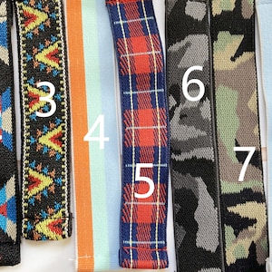 May include: A collection of nine colorful elastic straps. Designs include geometric patterns, camouflage, plaid, and stripes. The straps are in various colors, including black, blue, green, orange, and pink. These straps are likely for crafting or accessories.