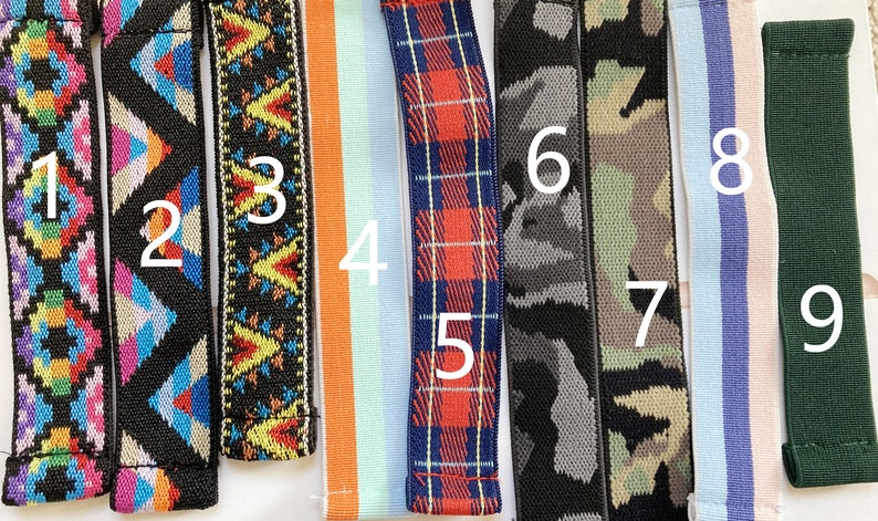 May include: A collection of nine colorful elastic straps. Designs include geometric patterns, camouflage, plaid, and stripes. The straps are in various colors, including black, blue, green, orange, and pink. These straps are likely for crafting or accessories.
