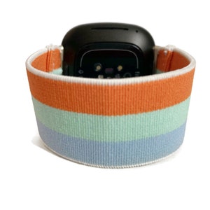 May include: A striped watch band with orange, light blue and dark blue stripes. The band is made of a soft, stretchy material.