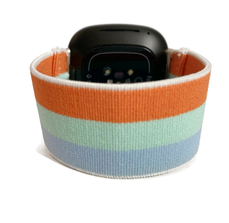 May include: A striped watch band with orange, light blue and dark blue stripes. The band is made of a soft, stretchy material.