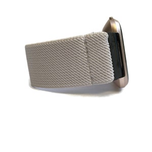 May include: A light gray elastic watch band with a rose gold watch face.