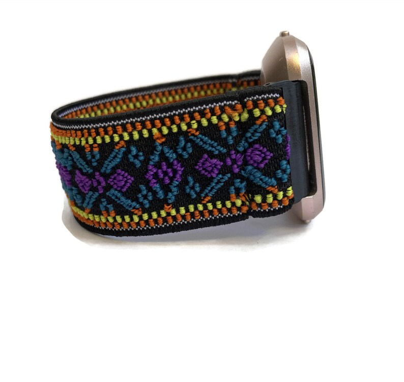 K&ouml;nnte beinhalten: Ein schwarzes elastisches Armband mit einem bunten geometrischen Muster in Orange-, Gelb-, T&uuml;rkis-, Lila- und Wei&szlig;t&ouml;nen. Das Armband ist an einer silbernen Smartwatch befestigt.