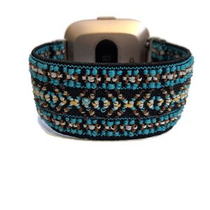 May include: A black elastic watch band with a turquoise, brown, and white geometric pattern. The band is designed for a smartwatch.