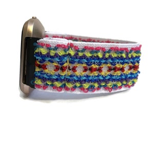May include: A white watch strap with a colourful embroidered pattern. The strap is made of a soft, stretchy material and features a variety of colours, including red, yellow, blue, green, and purple.