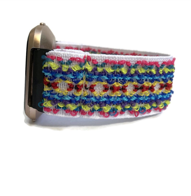 May include: A white watch strap with a colourful embroidered pattern. The strap is made of a soft, stretchy material and features a variety of colours, including red, yellow, blue, green, and purple.