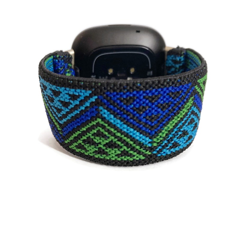 May include: A black smartwatch with a blue, green, and black patterned band. The band is made of woven fabric.