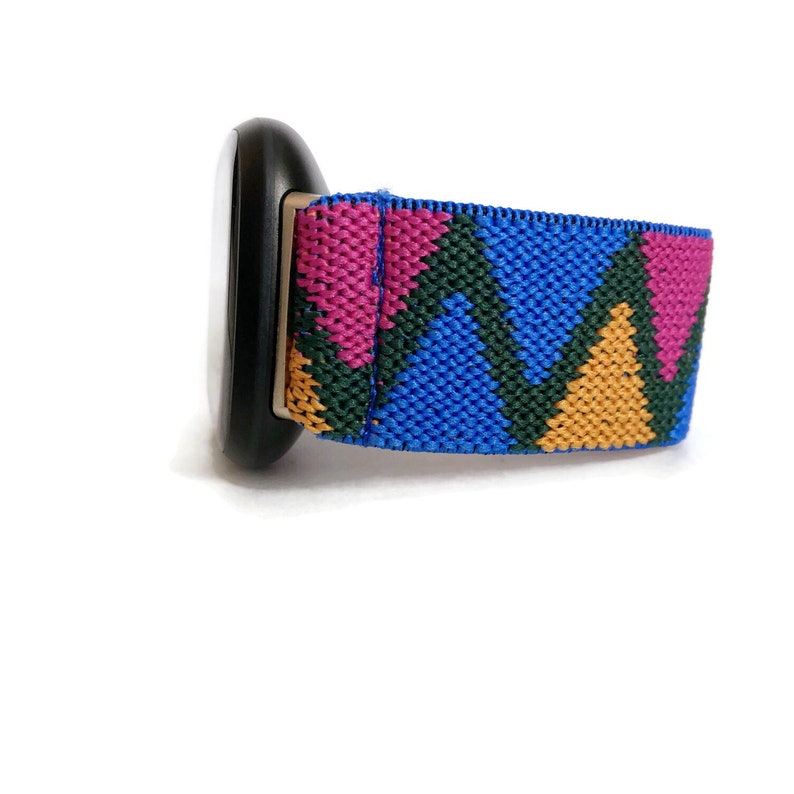 May include: A blue, green, pink, and yellow patterned watch band. The band is made of a woven fabric and has a geometric design.