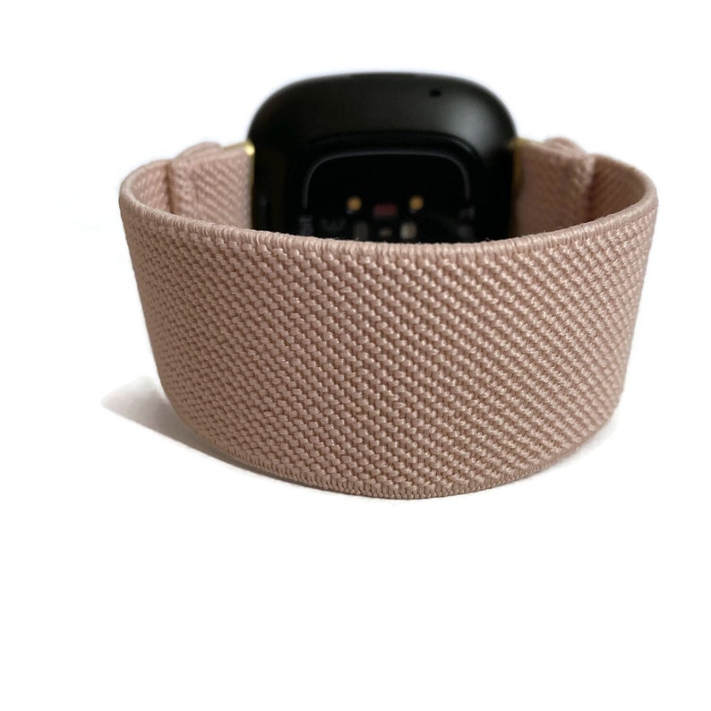 May include: A light pink elastic watch strap with a black watch face. The strap is made of a soft, textured material.