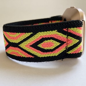 May include: A black elastic watch band with a geometric pattern in pink and green. The band is attached to a silver watch face.