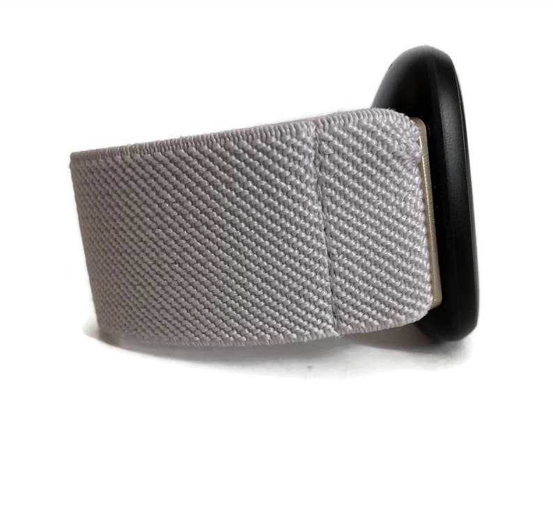 May include: A gray fabric watch band with a black circular watch face.
