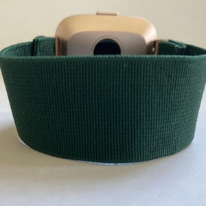 Op de afbeelding: Een donkergroen horlogebandje gemaakt van zacht, getextureerd materiaal. Het bandje is ontworpen om te passen op een smartwatch met een gouden kast.