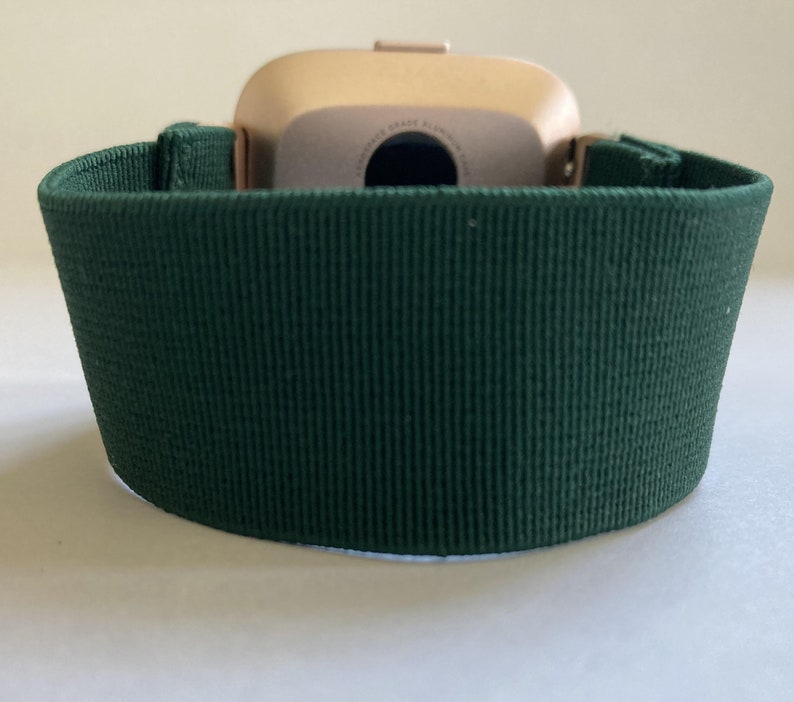 Op de afbeelding: Een donkergroen horlogebandje gemaakt van zacht, getextureerd materiaal. Het bandje is ontworpen om te passen op een smartwatch met een gouden kast.