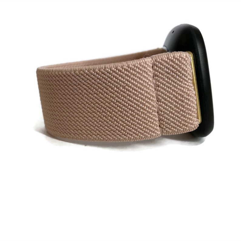 May include: A light pink elastic watch strap with a black and gold watch face.