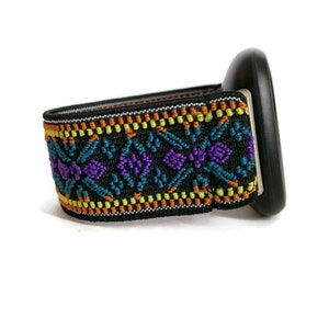 May include: A black watch band with a colorful geometric pattern in shades of orange, yellow, teal, and purple. The band is made of a stretchy material and has a black buckle.