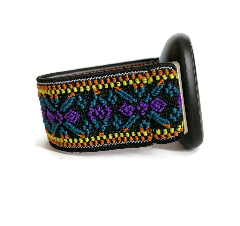 May include: A black watch band with a colorful geometric pattern in shades of orange, yellow, teal, and purple. The band is made of a stretchy material and has a black buckle.