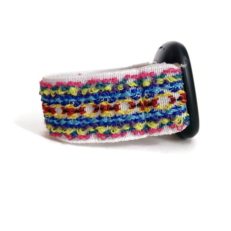 K&ouml;nnte beinhalten: Ein wei&szlig;es Armband mit einem bunten geometrischen Muster. Das Armband ist aus weichem, gewebtem Material und hat ein schwarzes Zifferblatt.