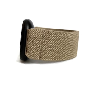K&ouml;nnte beinhalten: Ein beigefarbenes elastisches Armband mit einer schwarzen Metallschnalle.
