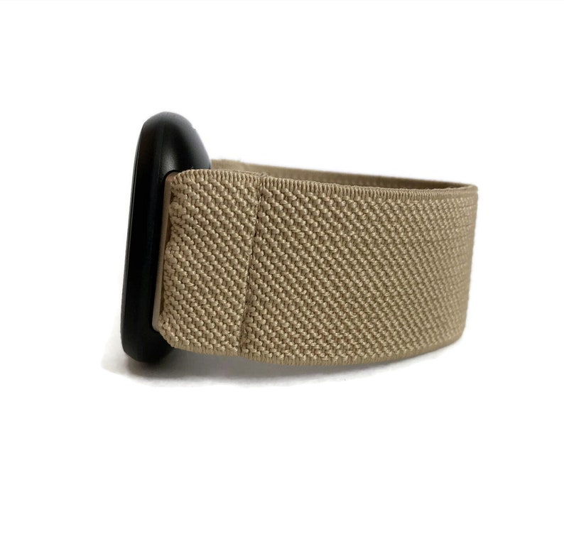 K&ouml;nnte beinhalten: Ein beigefarbenes elastisches Armband mit einer schwarzen Metallschnalle.