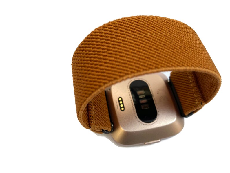 May include: A gold-colored fitness tracker with a brown fabric band. The tracker has a small screen and a few buttons on the side.
