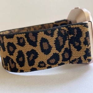 May include: A gold-colored smartwatch with a leopard print elastic band.