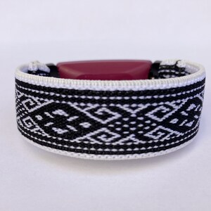 Peut inclure: Un bracelet tiss&eacute; avec un motif g&eacute;om&eacute;trique noir et blanc. Le bracelet a une pi&egrave;ce ma&icirc;tresse rectangulaire, rouge fonc&eacute;. Le bracelet mesure environ 2,5 cm de large.