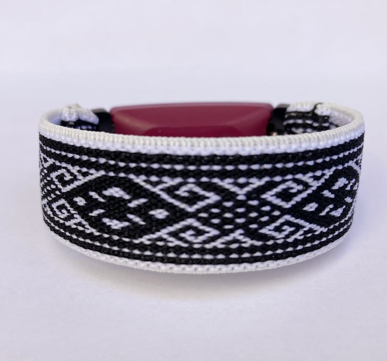 Peut inclure: Un bracelet tiss&eacute; avec un motif g&eacute;om&eacute;trique noir et blanc. Le bracelet a une pi&egrave;ce ma&icirc;tresse rectangulaire, rouge fonc&eacute;. Le bracelet mesure environ 2,5 cm de large.