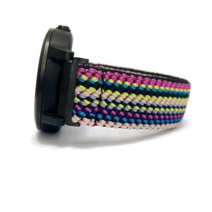 May include: A black watch with a multi-colored woven nylon strap. The strap features pink, blue, yellow, and black stripes.