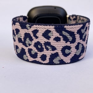 May include: A pink and navy blue leopard print watch band. The band is made of a soft, stretchy material and is compatible with smartwatches.