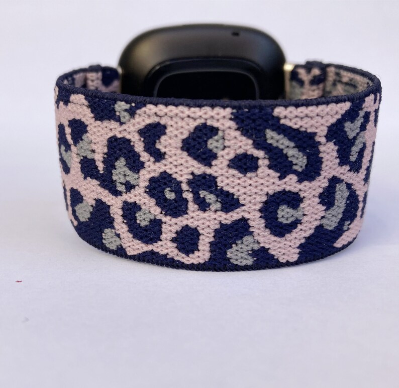 May include: A pink and navy blue leopard print watch band. The band is made of a soft, stretchy material and is compatible with smartwatches.