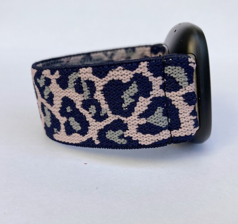 May include: A navy blue and pink leopard print watch band. The band is made of a stretchy material and is designed to fit a smartwatch.