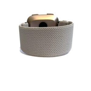 May include: A gray elastic band for a fitness tracker. The band is made of a soft, breathable material and has a textured surface.