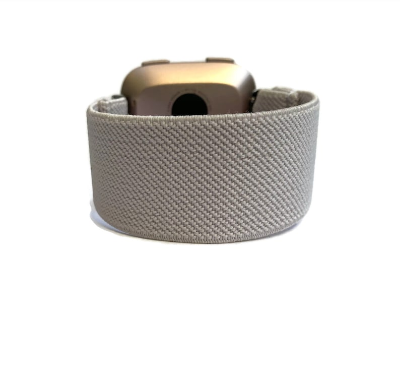 May include: A gray elastic band for a fitness tracker. The band is made of a soft, breathable material and has a textured surface.
